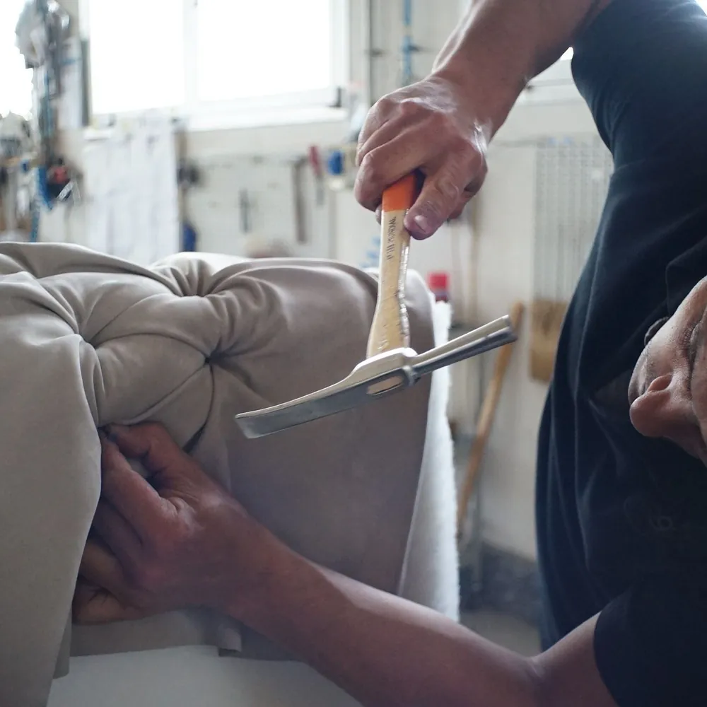 Manos trabajando con herramientas de tapicero sobre el asiento de un sofá en un taller